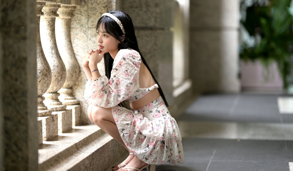 Красивая девушка азиатка в костюме сидит у стены