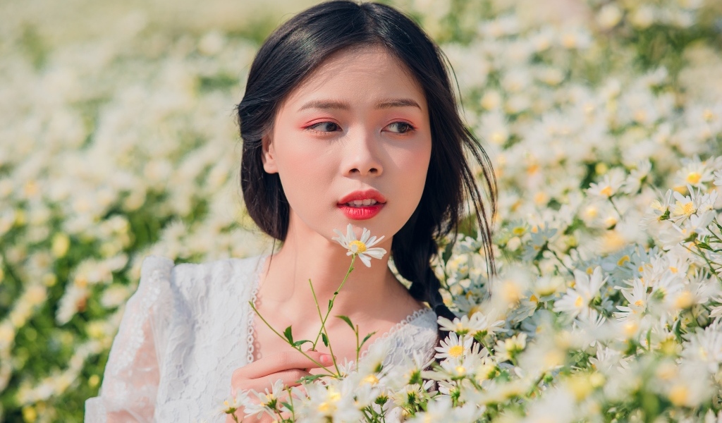 Красивая девушка азиатка на поле с белыми ромашками