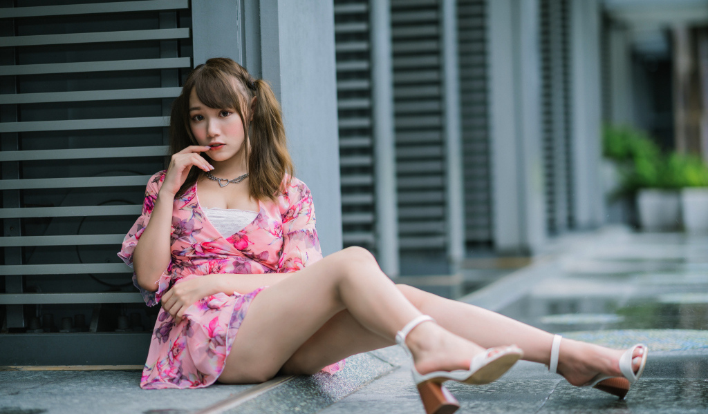 Красивая азиатка в розовом платье сидит у стены