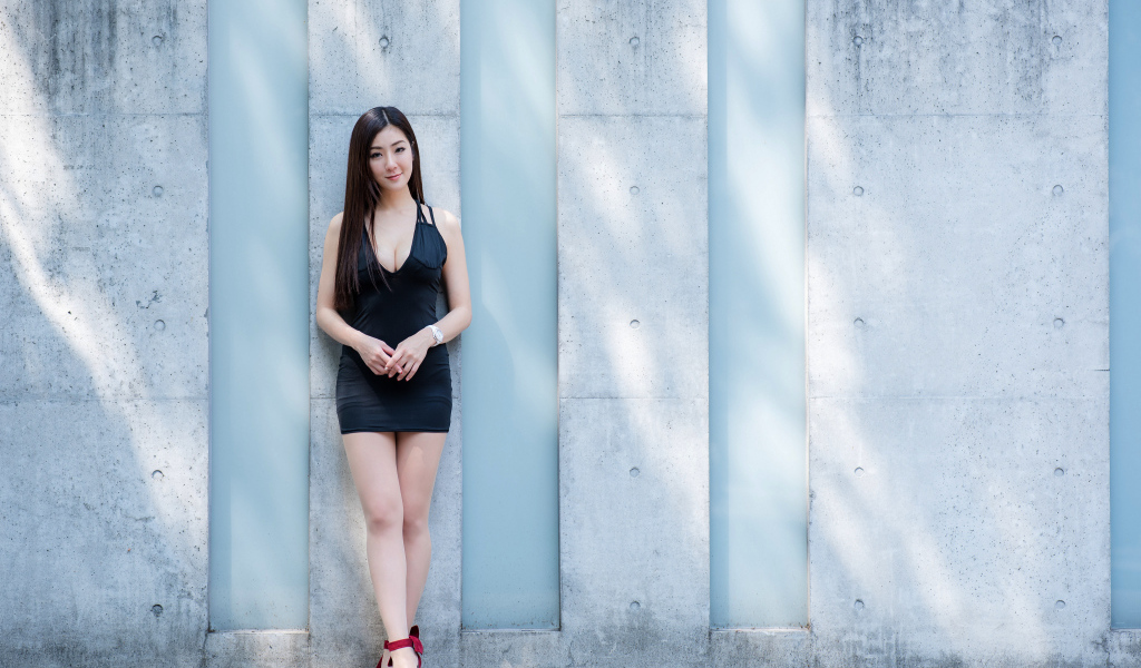 Красивая азиатка в коротком платье стоит у стены