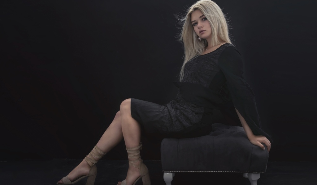 Красивая девушка в черном платье сидит на кресле