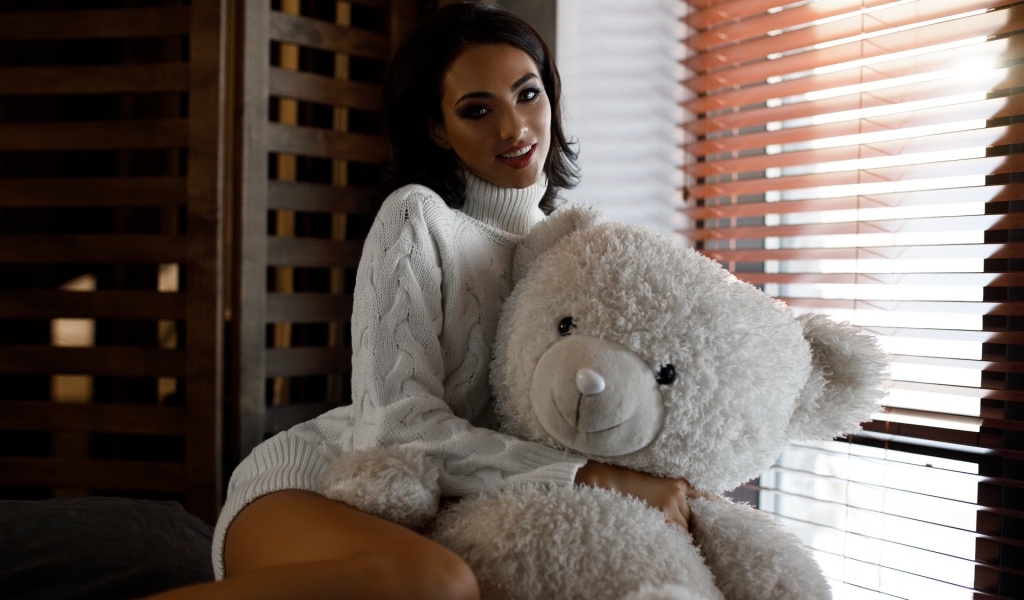 Красивая девушка в свитере с медведем у окна