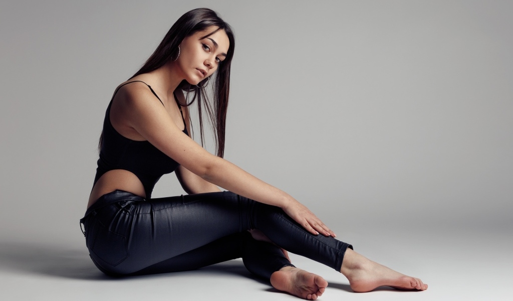 Красивая девушка в черных брюках на сером фоне