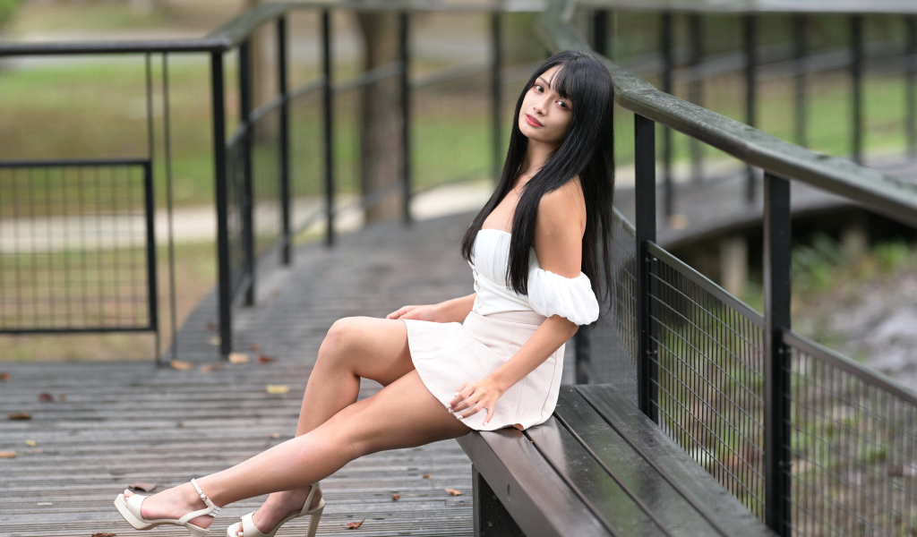 Красивая длинноволосая азиатка в белом платье сидит на лавке