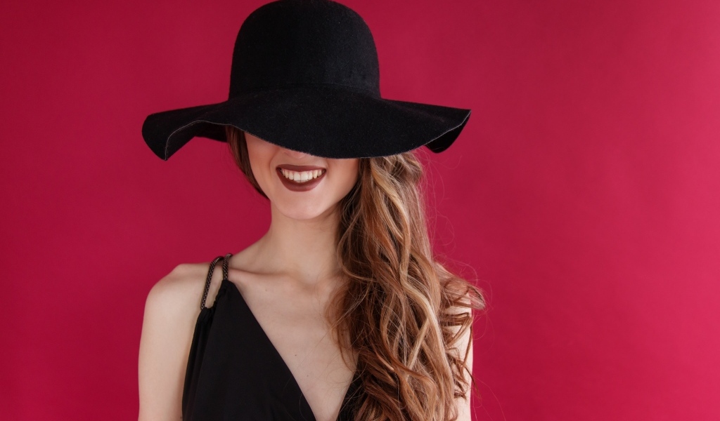 Черная шляпа на лице у девушки на розовом фоне