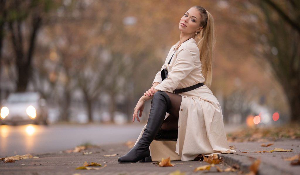Девушка блондинка сидит в пальто в парке