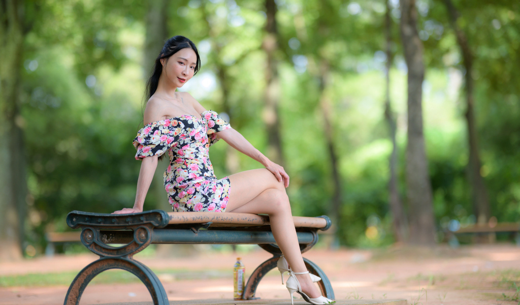 Милая девушка азиатка в платье сидит на лавке в парке