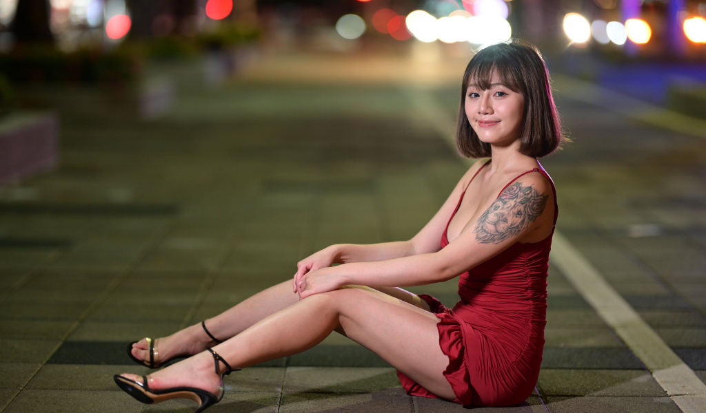 Милая азиатка в красном платье сидит на дороге
