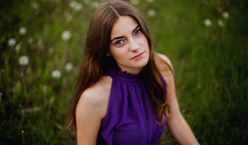 Милая девушка в фиолетовом платье сидит на траве