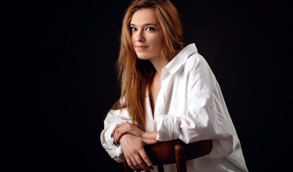 Милая девушка в белой рубашке сидит на стуле