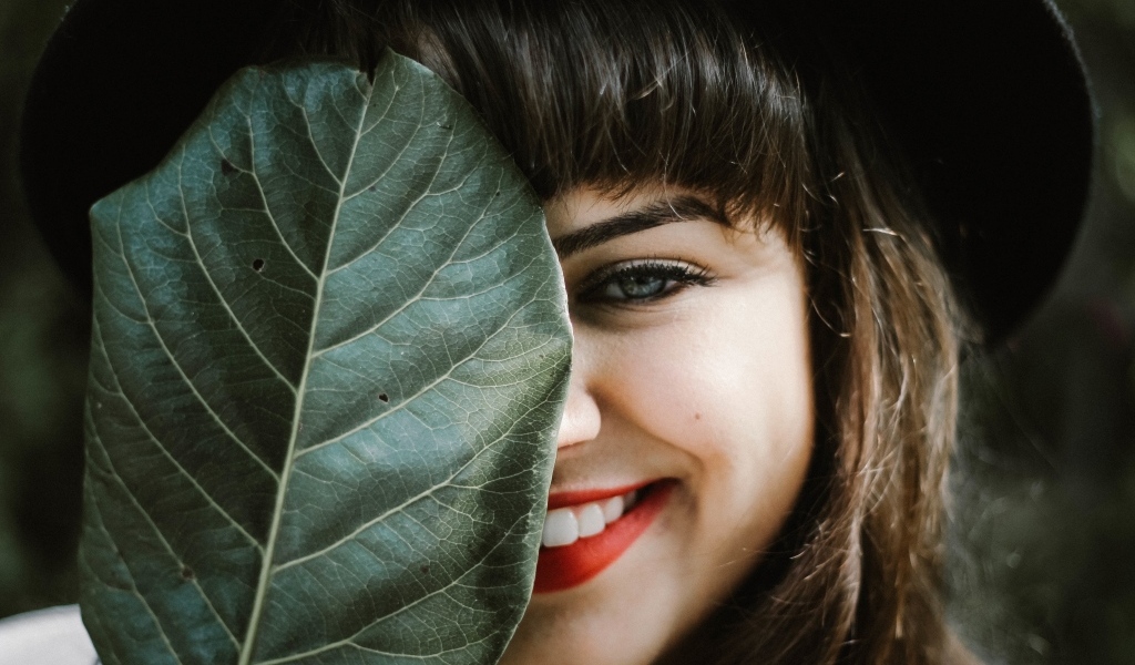 Милая улыбающаяся девушка прикрыла лицо листом