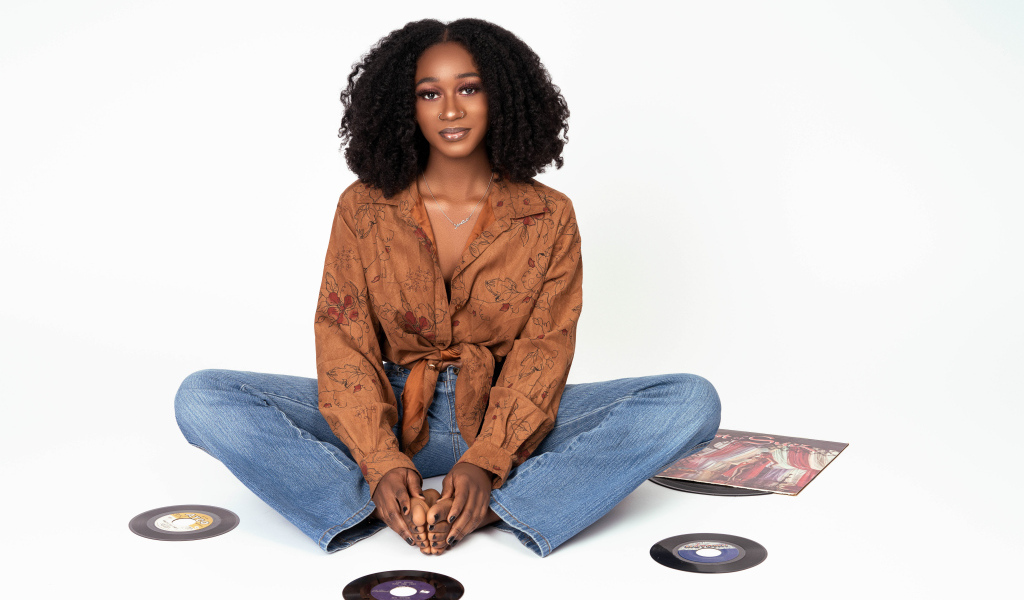 Темнокожая девушка сидит на белом фоне с пластинками