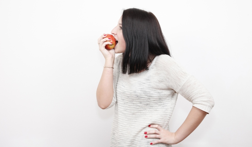 Девушка кусает красное яблоко 