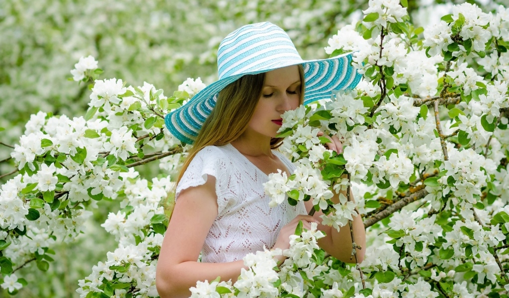 Девушка в шляпе нюхает ветку яблони 
