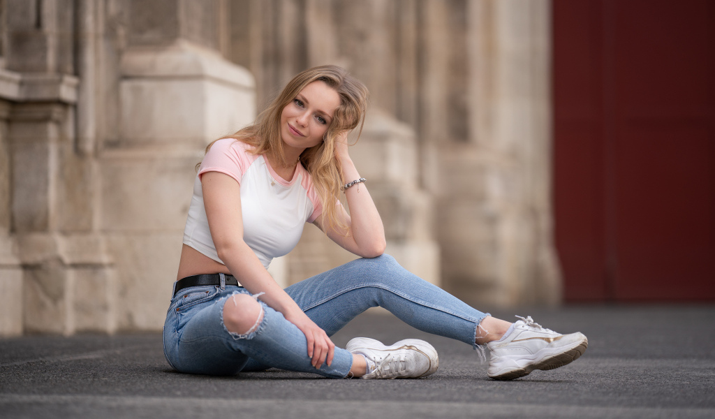 Девушка в рваных джинсах сидит на асфальте