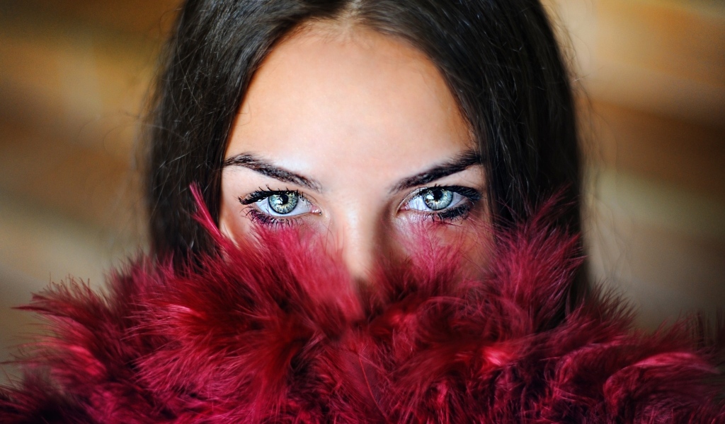Девушка с красивыми глазами закрыла лицо красными перьями