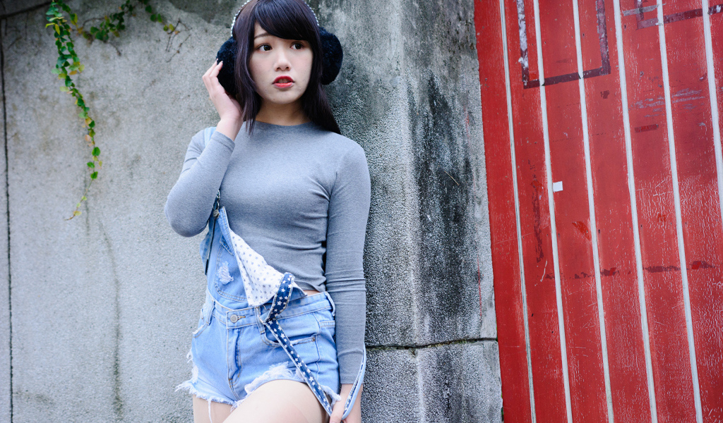 Скромная девушка азиатка в наушниках стоит у стены