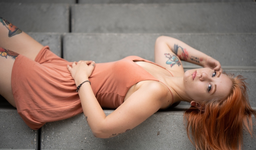 Рыжеволосая девушка с татуировками лижет на ступеньках