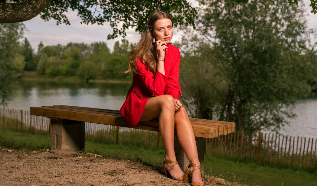 Грустная девушка в красном пальто сидит на лавке