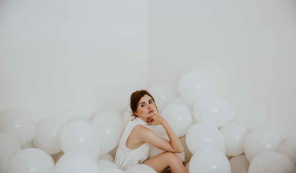 Грустная девушка сидит в белых воздушных шариках