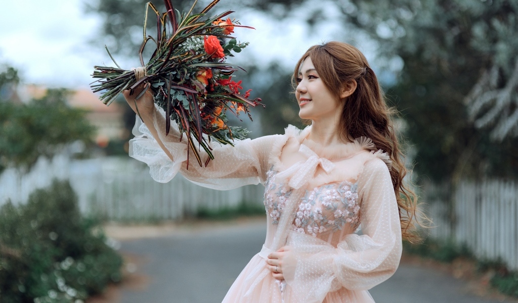 Улыбающаяся девушка азиатка в розовом платье с букетом