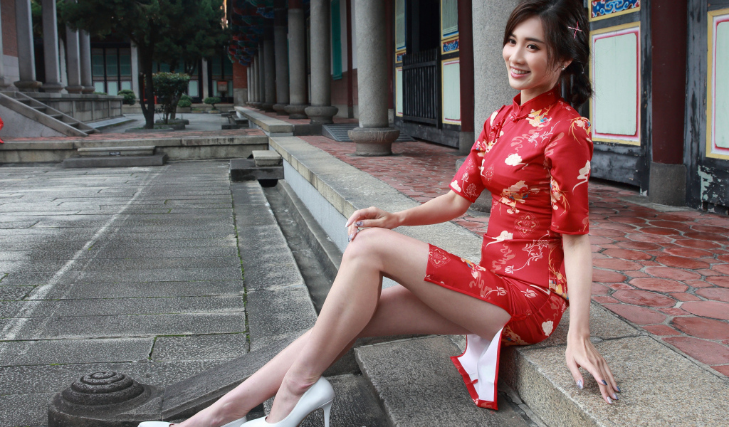 Улыбающаяся девушка азиатка в красном платье сидит на ступеньках