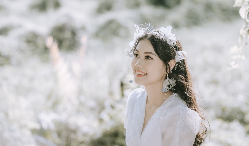 Улыбающаяся девушка азиатка в белом платье на поле