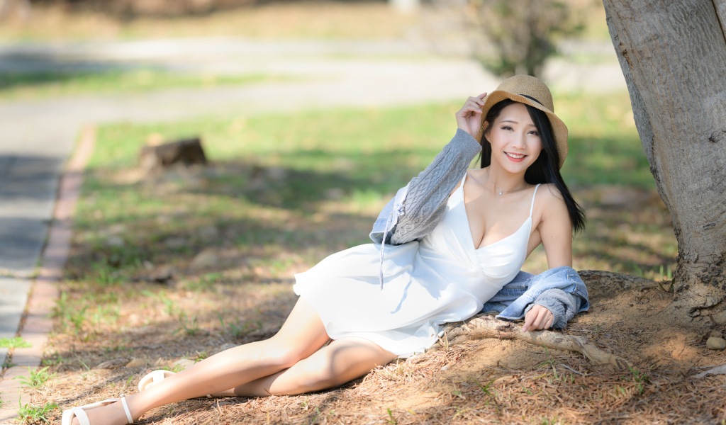 Улыбающаяся азиатка в белом платье лежит под деревом