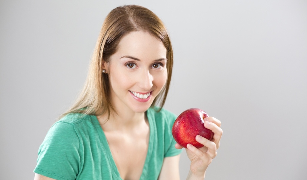 Улыбающаяся девушка с красным яблоком в руках