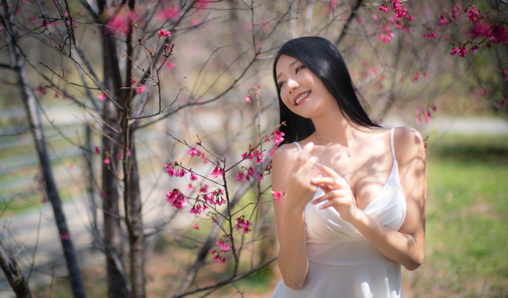 Улыбающаяся девушка в белом платье у дерева с цветами