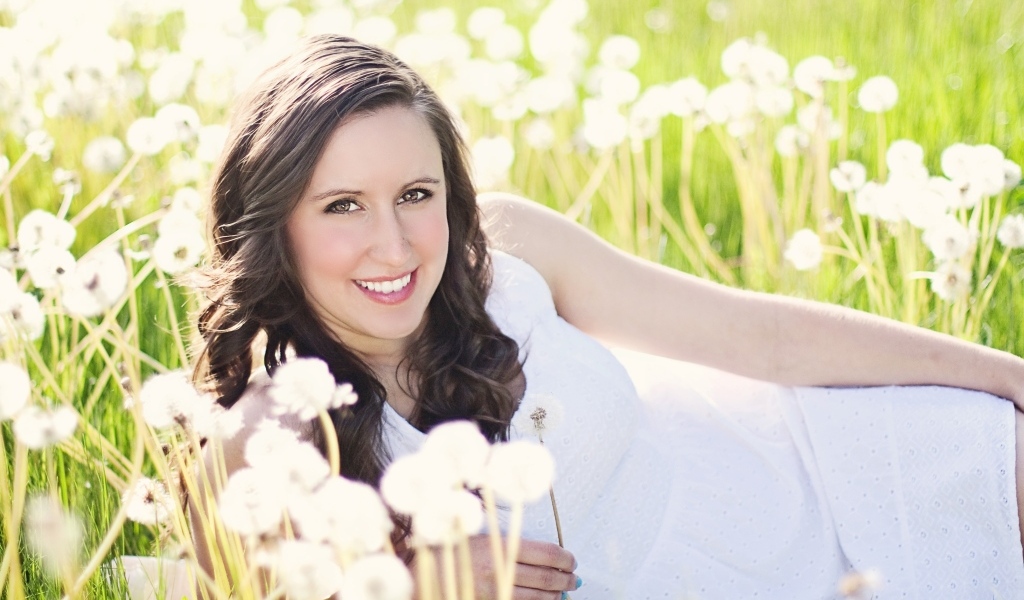 Улыбающаяся девушка лежит на поле с одуванчиками