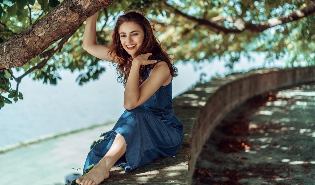 Улыбающаяся девушки сидит у дерева