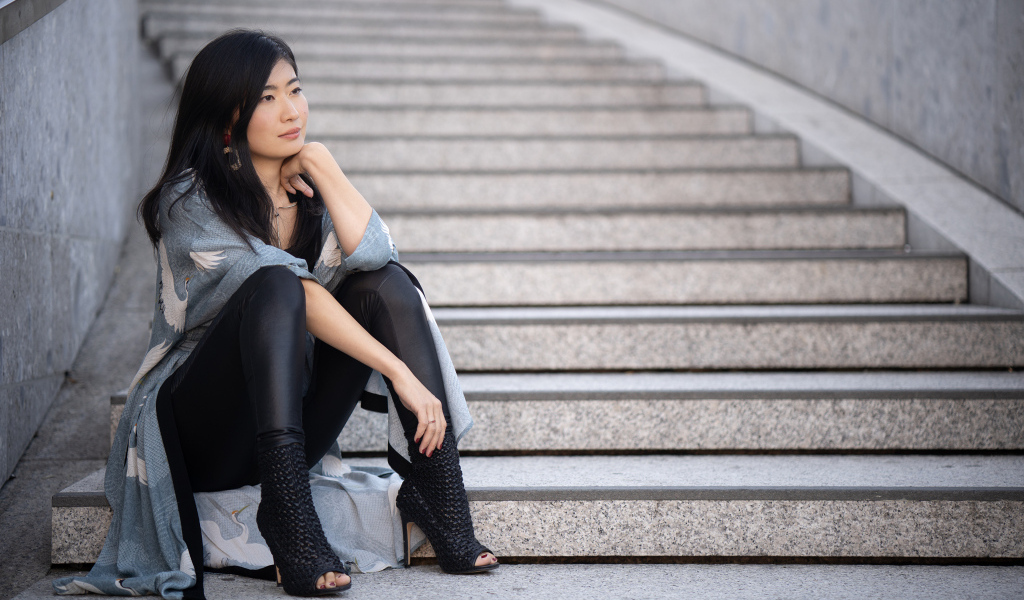 Задумчивая девушка азиатка сидит на ступеньках
