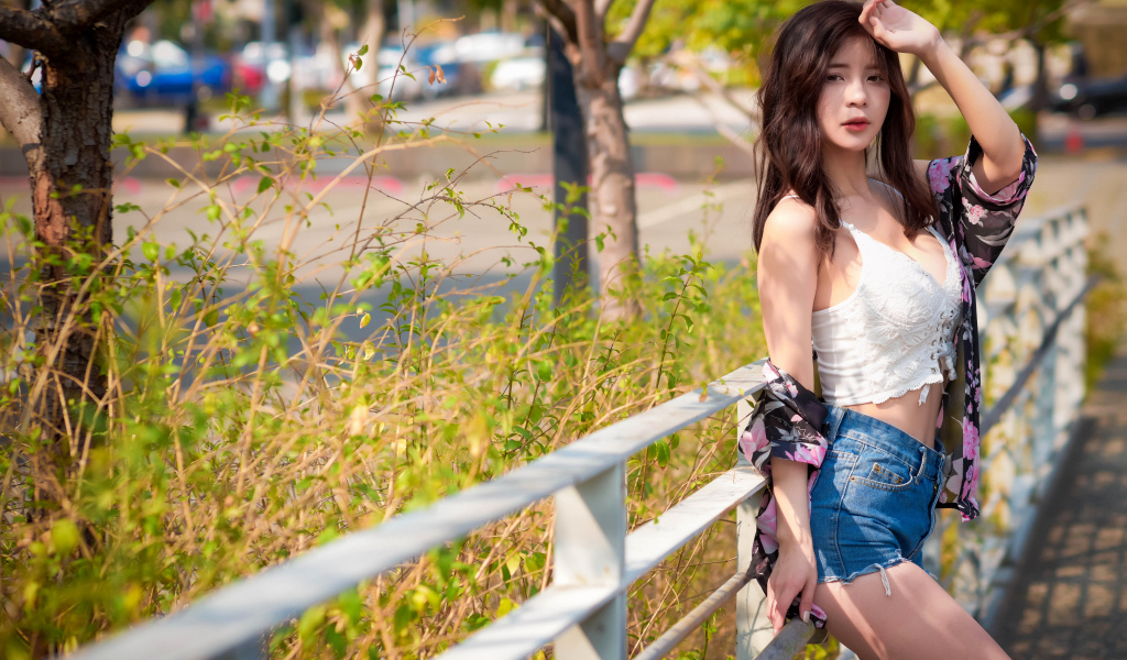 Молодая азиатка в синих шортах стоит у забора