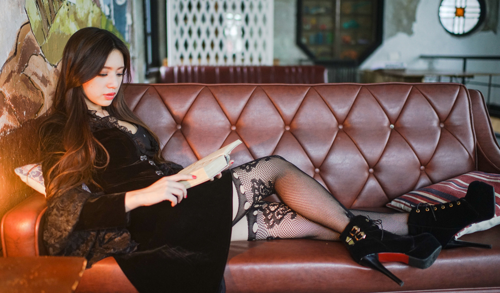Молодая девушка читает книгу на кожаном диване