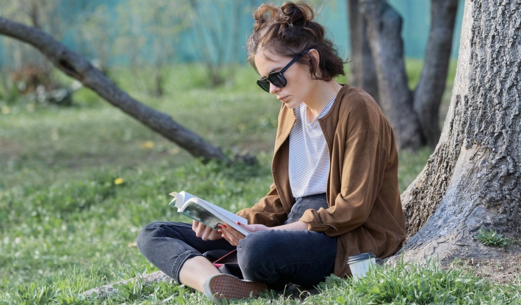 Молодая девушка сидит под деревом с книгой