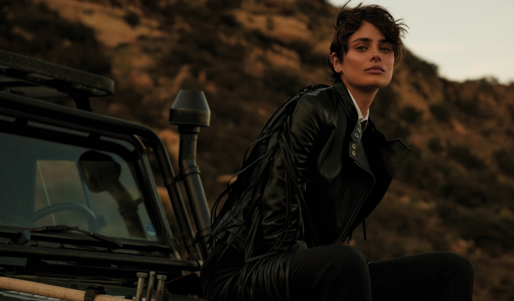 Модель Тейлор Хилл в черной куртке сидит на машине