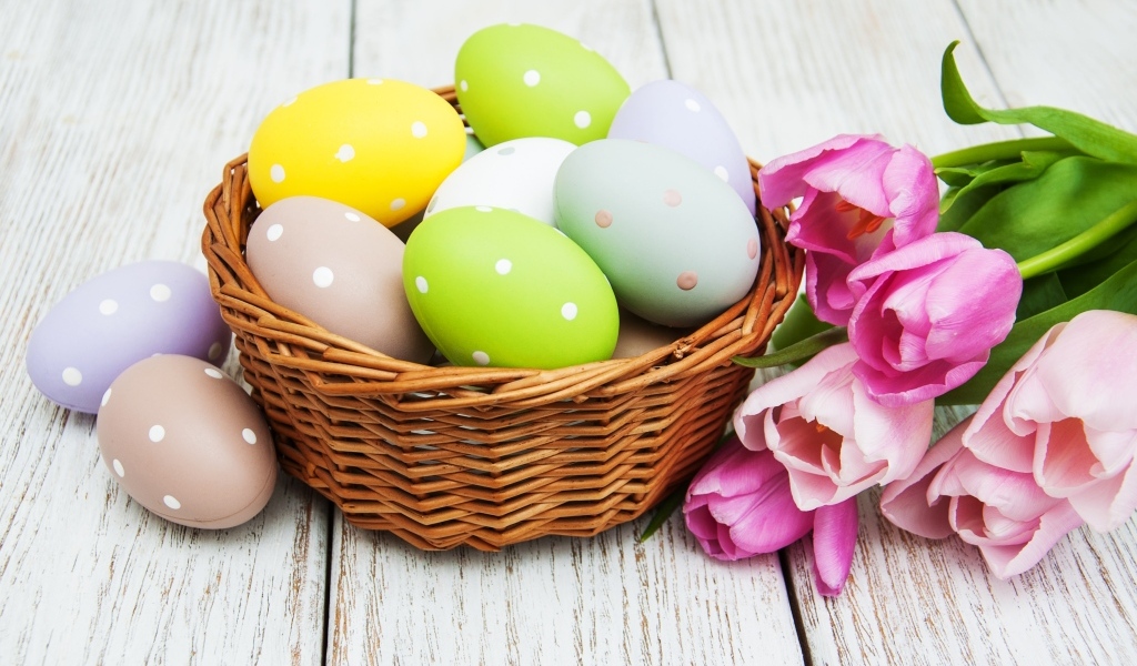 Корзина разноцветных яиц с тюльпанами на столе на Пасху