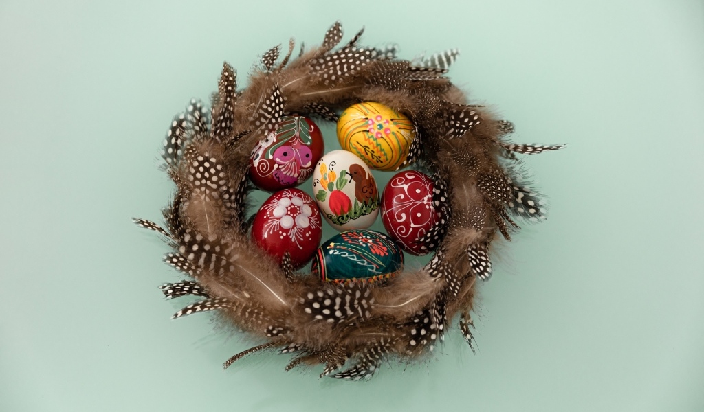 Красивые разноцветные яйца в гнезде из перьев на сером фоне