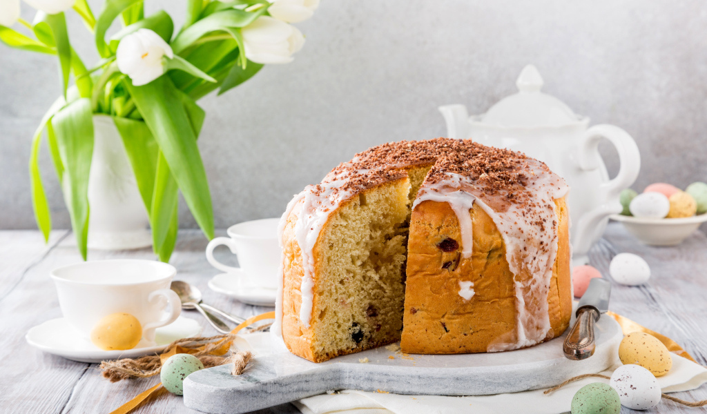 Пасхальный кулич на столе с букетом тюльпанов и сладостями