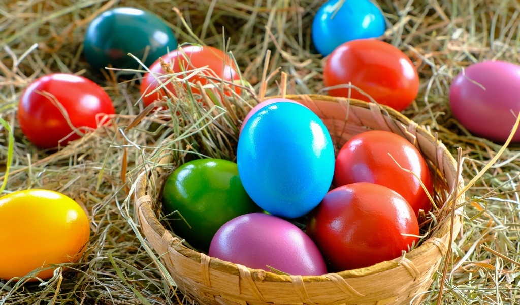 Разноцветные пасхальные яйца в корзине на сене