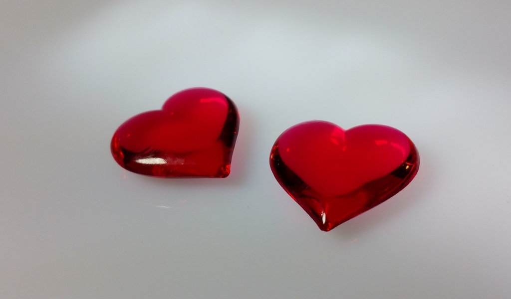 Два красных стеклянных сердца на сером фоне