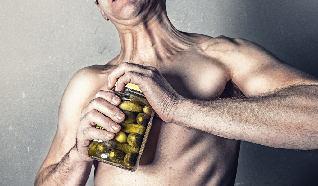 Мужчина открывает банку огурцов