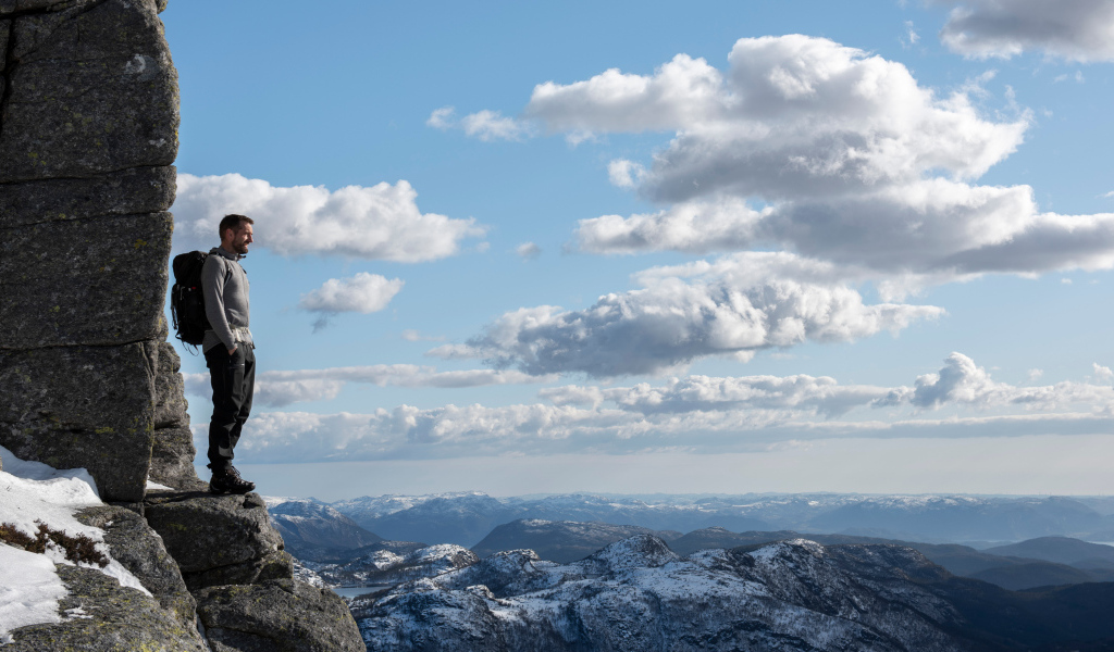 Мужчина стоит на краю скалы на фоне неба 