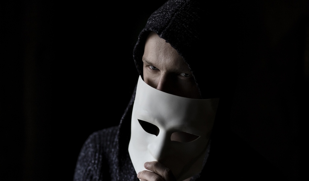 Мужчина с белой маской в руке на черном фоне