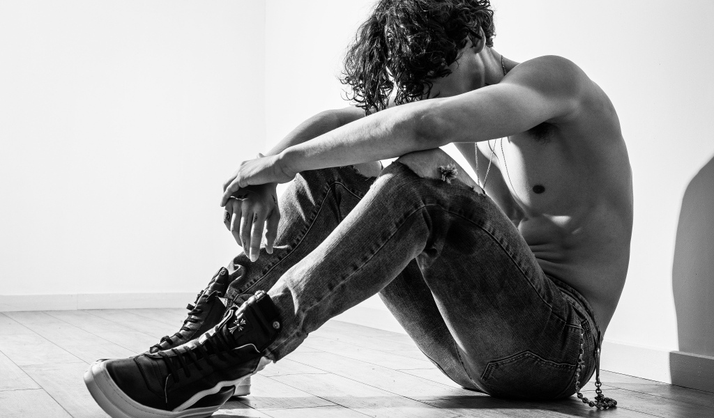 Грустный мужчина в джинсах сидит на полу