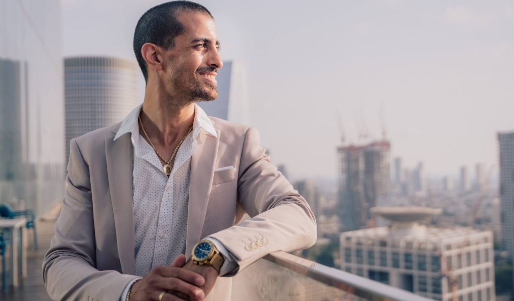 Улыбающийся стильный мужчина в костюме стоит на балконе 