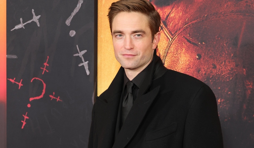 Популярный актер Роберт Паттинсон в костюме стоит у стены