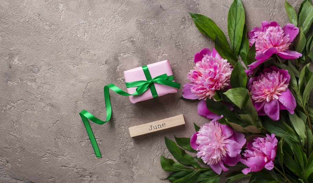 Букет розовых пионов с подарком на сером столе