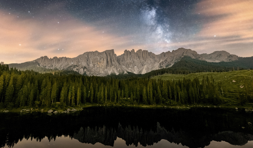 Млечный путь над горами и лесом отражающимися в воде